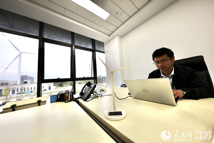 在寧海峰的辦公室內，桌面的太陽能風機紀念品與窗外的大型風機相映成趣。 人民網 馬燾燾攝