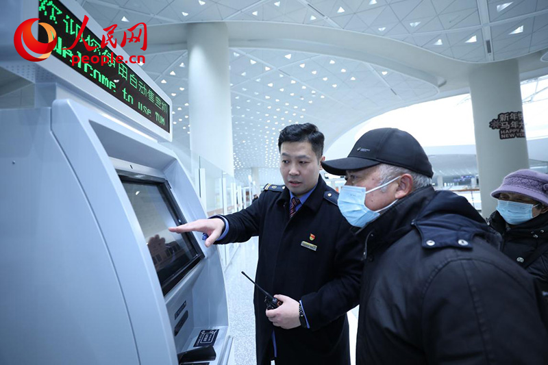 1月4日,在北京通州站,邵辰飞(左)帮助旅客使用自助购票机。人民网记者 尹星云摄